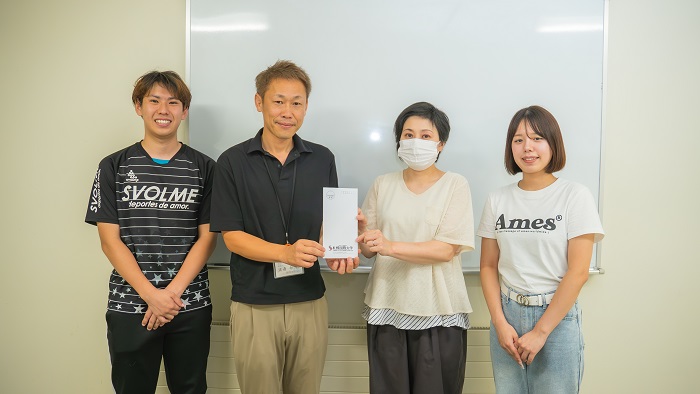 子ども食堂の方に売上金の一部を手渡す学生